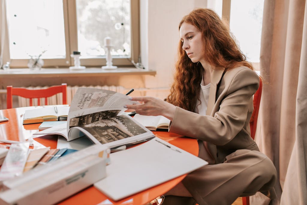 A focused woman in a beige suit reading documents at a desk in a modern office setting.