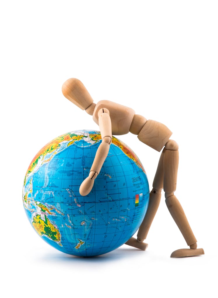 A wooden mannequin pushes a blue globe isolated on white background.