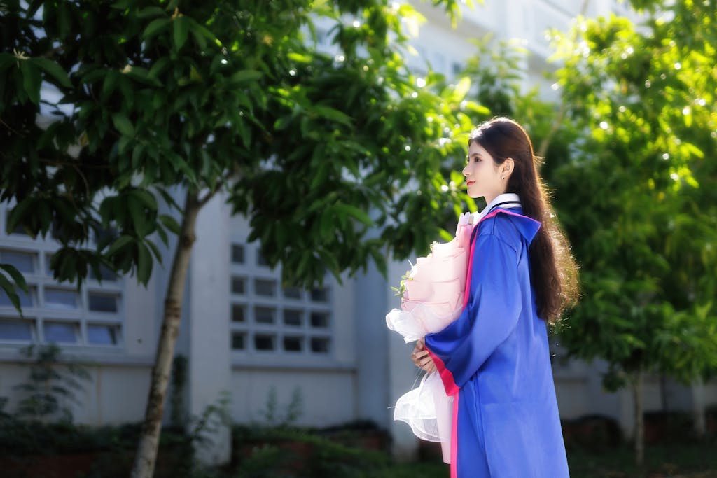 A young woman in graduation gown holding a bouquet outdoors, celebrating her accomplishment.