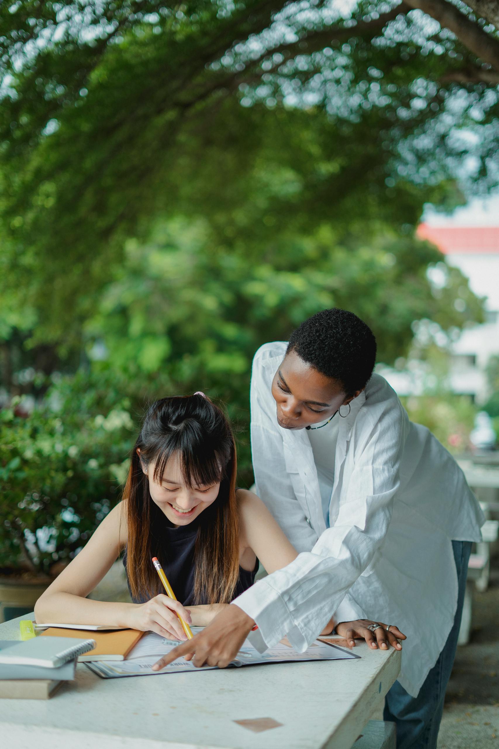 Young multiracial women studying with books outside together and wearing casual clothes in summer day at table